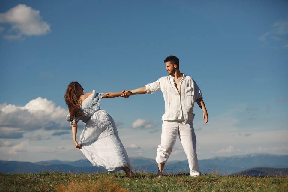 A joyful couple dancing in nature, enjoying a sunny summer day outdoors.