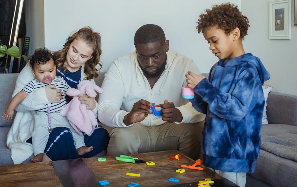Black kid playing toys with father sitting on sofa near wife hugging cute baby while spending time together