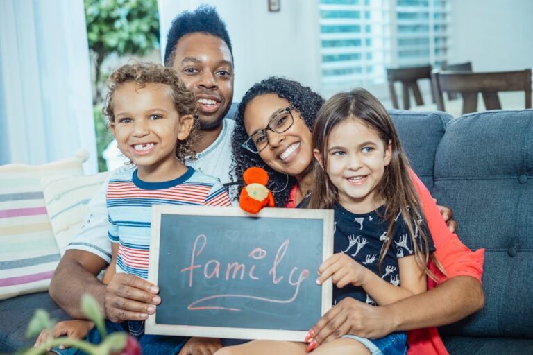 Smiling family of four indoors holding a blackboard with 'family' written on it.