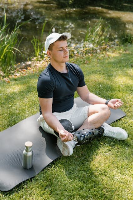 A man with prosthetic leg meditating on a yoga mat outdoors, symbolizing peace.