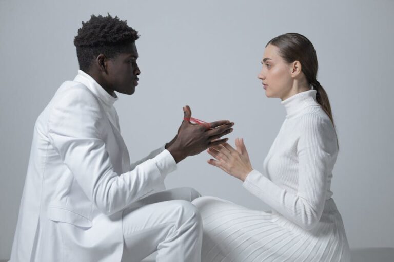 Two people in white outfits engage in conversation indoors; minimalism theme.
